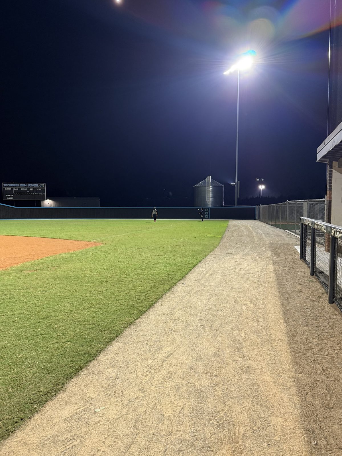 Two ORIGIN athletes in right field under the lights, seen down the right-field line.